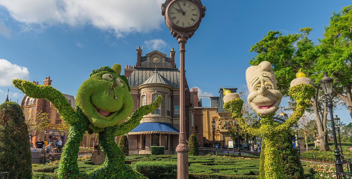 In the France pavilion, topiaries of Cogsworth and Lumiere from Beauty and the Beast stand next each other. Cogsworth lifts a leg in the air with his arms flung out while Lumiere holds his candle hands up. A tall, silver clock sits between them.