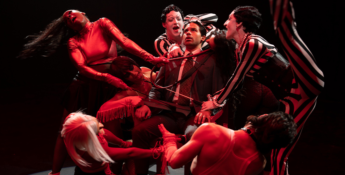 In a scene from Up Here, Miguel, played by Carlos Valdes, is part of a cabaret performance. He is surrounded by seven dancers and appears to be stressed.