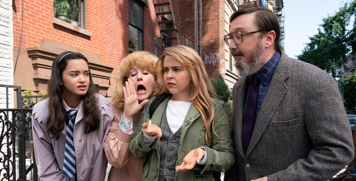 In a scene from an episode of Up Here actors Sophia Hammons, Katie Finneran, Mae Whitman, and John Hodgman stand huddled together on a New York City sidewalk.