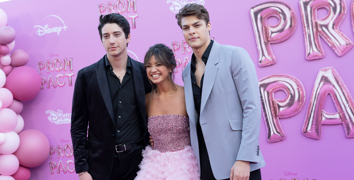 Milo Manheim, Peyton Elizabeth Lee, and Blake Draper pose for a photo at the Prom Pact premiere. The backdrop is pink and there are pink balloons to their left.