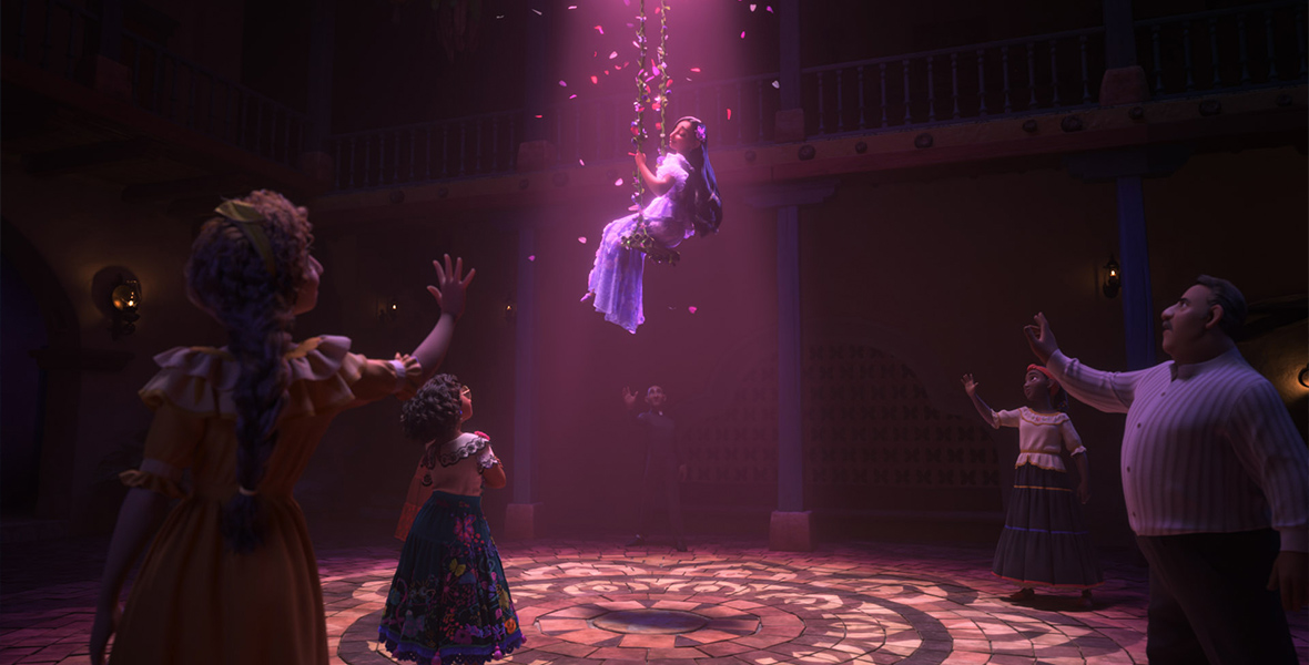 In a scene from Encanto, Isabela sits on a swing made of flowers and is bathed in purple light. Her family members stand below, extending their arms.