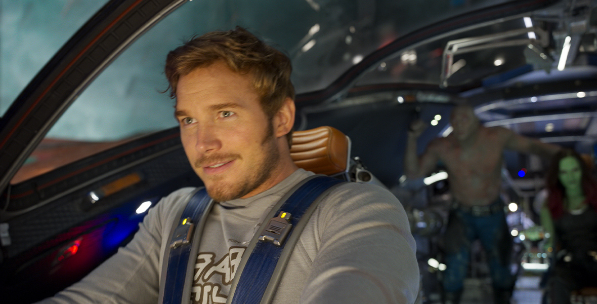 In Guardians of the Galaxy Vol. 2, Peter Quill pilots a ship. He smiles as he steers, while Gamora and Drax are blurry in the background.