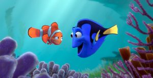 Marlin, an orange clownfish, and Dory, a blue tang, look at each other while floating above purple sea anemones. Marlin is looking with skeptical amusement at Dory’s enthusiastic, wide grin.