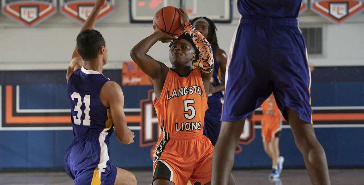 In a scene from an episode of The Crossover, actor Jalyn Hall attempts a shot during a basketball game and wears an orange jersey and matching orange shorts.
