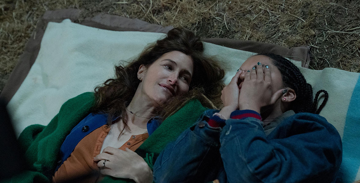 Clare, played by Kathryn Hahn, looks at her daughter, Rae, played by Tanzyn Crawford, who is covering her eyes. They are both lying on a blanket, outside, at night.