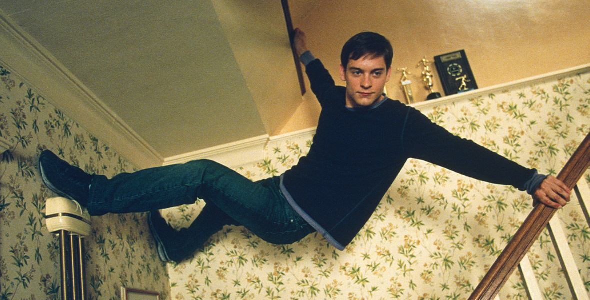 In a scene from Spider-Man, actor Tobey Maguire plays Peter Parker and hangs upside down on a home staircase.