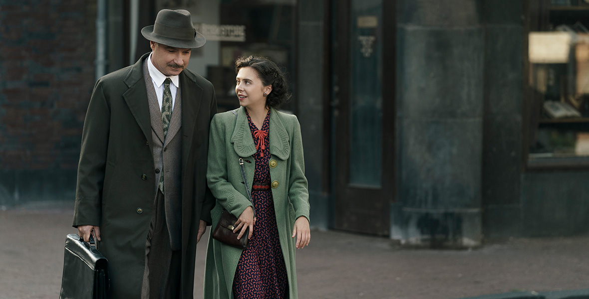 In a scene from A Small Light, Bel Powley as Miep Gies and Liev Schreiber as Otto Frank walk down a cobblestone street in Amsterdam.