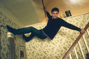 In a scene from Spider-Man, actor Tobey Maguire plays Peter Parker and hangs upside down on a home staircase.