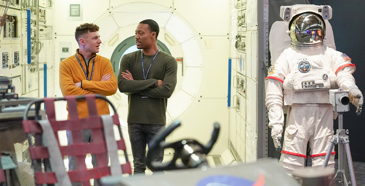 In a scene from Abbott Elementary, actors Tyler James Williams and Chris Perfetti stand in a NASA exhibit at the Franklin Institute.