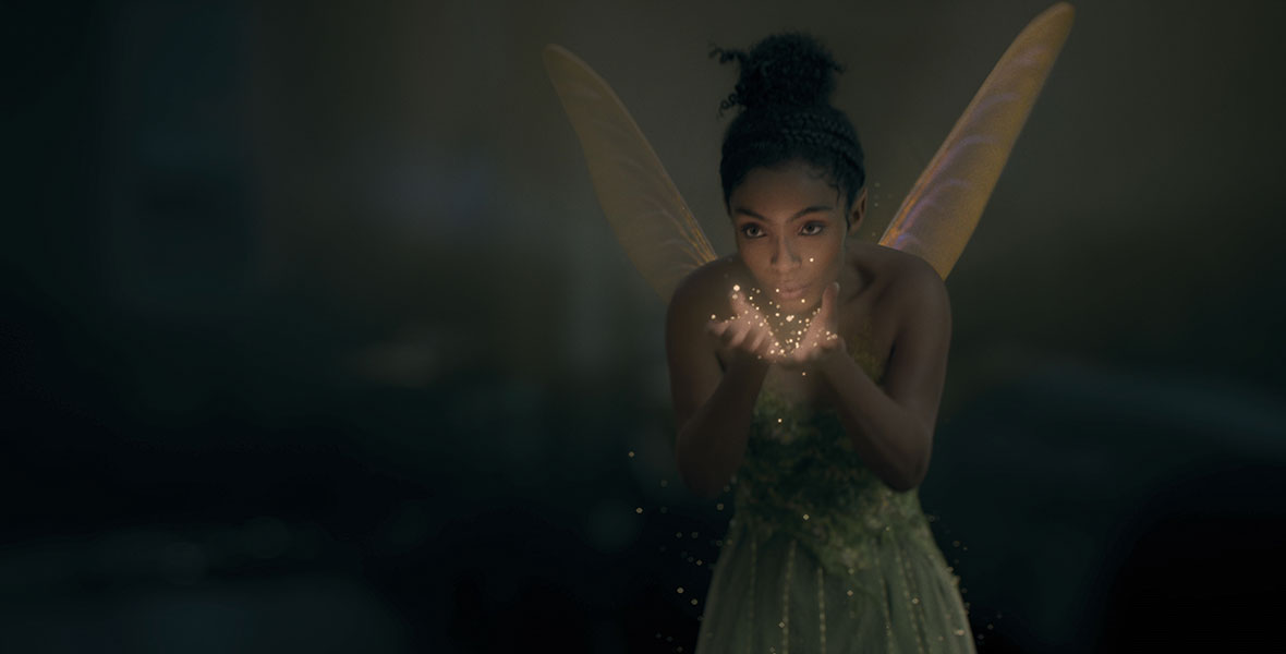 A still of the enchanting Tinker Bell, who blows pixie dust out of her palms. She wears a whimsical green dress, and her hair is swept above her head. Her dainty wings flutter.