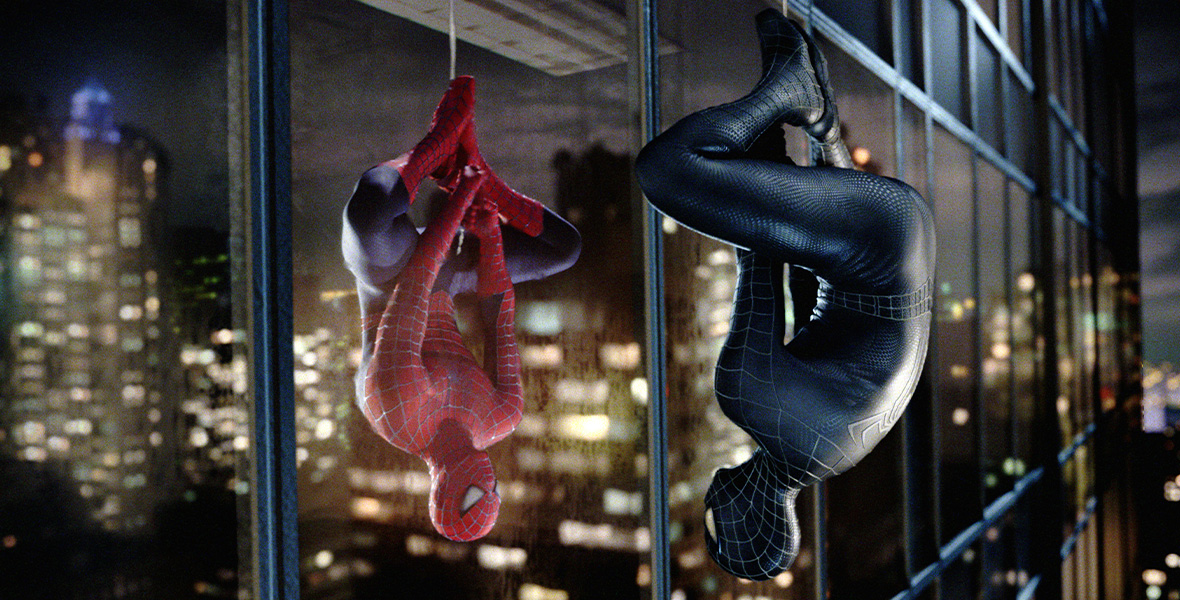 In a scene from Spider-Man 3, Spider-Man wears a black superhero suit and dangles upside down, looking at his reflection in a skyscraper window.