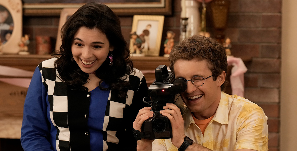 In a scene from The Goldbergs, actor Sean Giambrone plays Adam Goldberg and holds a video camera and stands next to actor Isabella Gomez as Carmen.