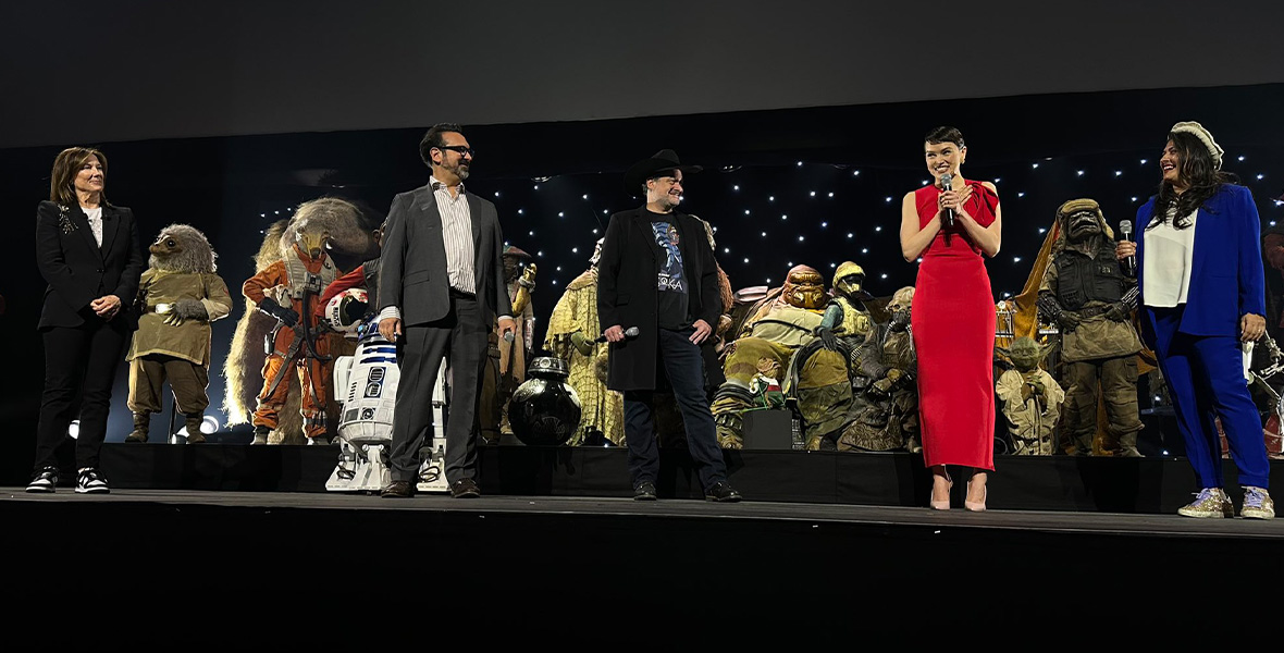 Kathleen Kennedy, James Mangold, Dave Filoni, Daisy Ridley, and Sharmeen Obaid-Chinoy onstage at the Lucasfilm Studio Showcase at Star Wars Celebration Europe. Behind them are an array of Star Wars aliens and droids.