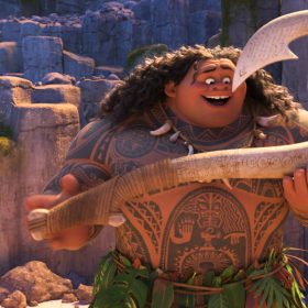 Moana (left), a teenage girl, smiles as she looks a Maui (right), a tattooed demigod, as he smiles and holds a giant, magical hook in both hands.