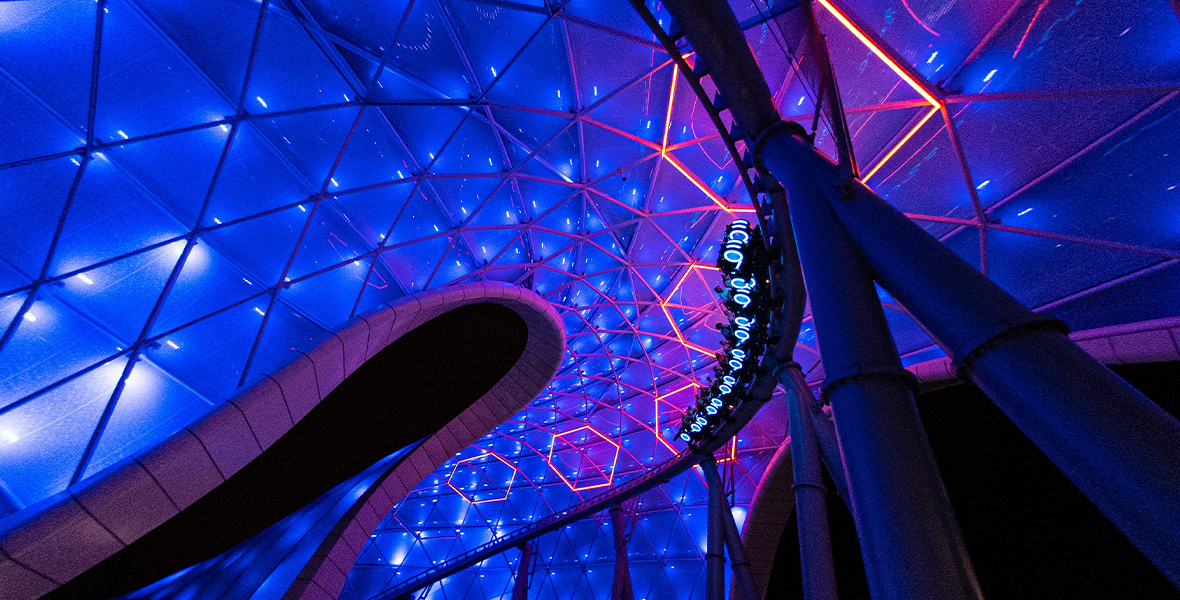 A train of Lightcyles traverse the indoor portion of the illuminated track at night.