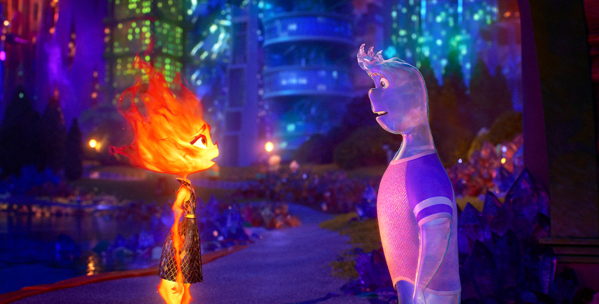 In a scene from the Pixar Animation Studios feature Elemental, Ember, a female fire person, stands facing Wade, a male water person, on a nighttime street with the colorful building of Element City behind them.