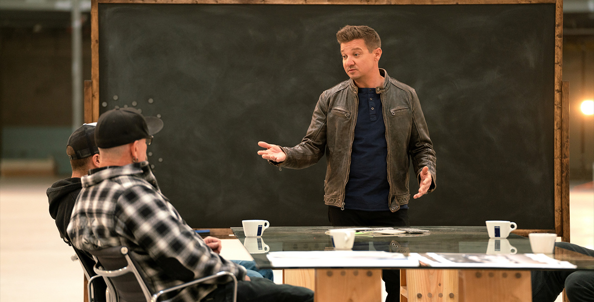 In a scene from Rennervations, actor Jeremy Renner stands in front of a chalk board during a presentation.