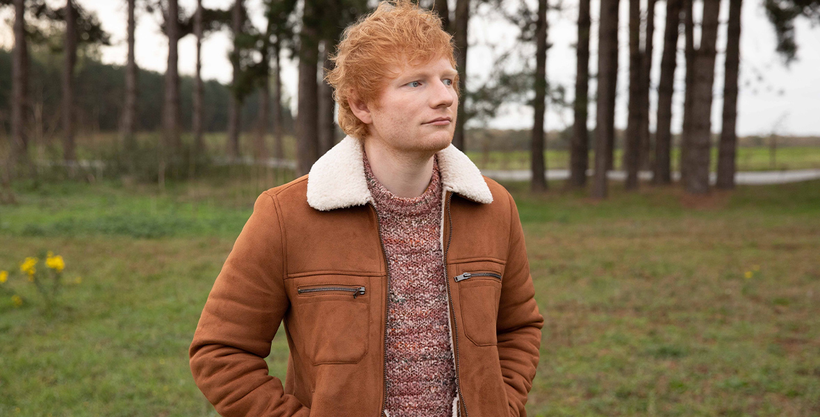 Ed Sheeran stands in a grassy field in a still from Ed Sheeran: The Sum of It All.