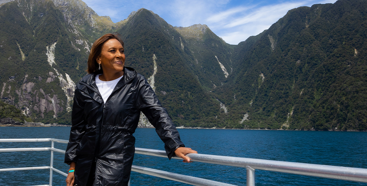 Robin Roberts smiles while holding onto the railing of a boat. She is on assignment in New Zealand and is wearing a black raincoat, a white T-shirt, and jeans.