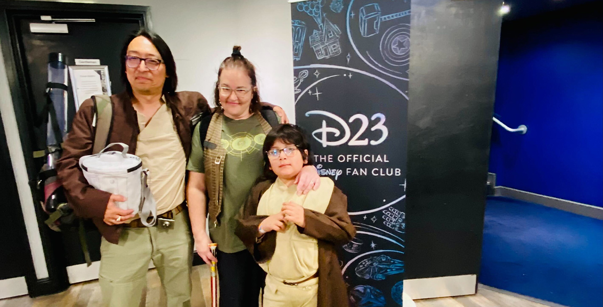 Excited D23 Members, dressed in their best Star Wars inspired gear, posed for a picture in front of a D23 sign.