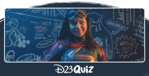 Kamala Khan, dressed as her hero alter ego Ms. Marvel, smiles while holding a piece of chalk. She is standing in front of a chalkboard with a variety of illustrations and plans drawn on it.