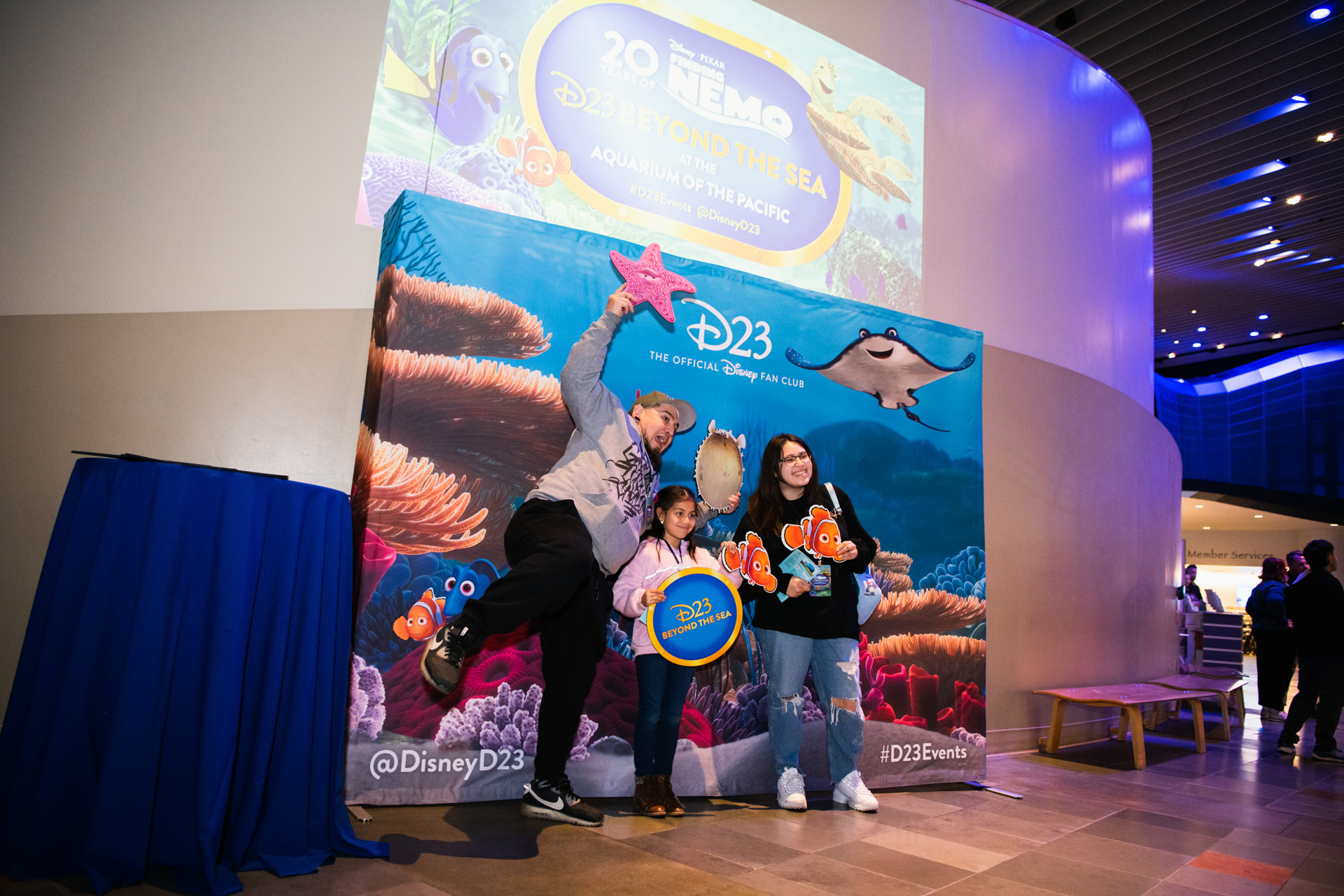 D23 Members smile and pose in front of a special photo opportunity that features characters from the movie, including Marlin and Dory.