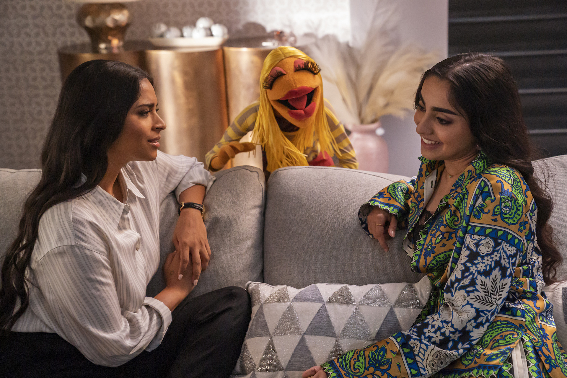 In a scene from The Muppets Mayhem, actors Lilly Singh and Saara Chaudry sit on a couch and chat with Janice.