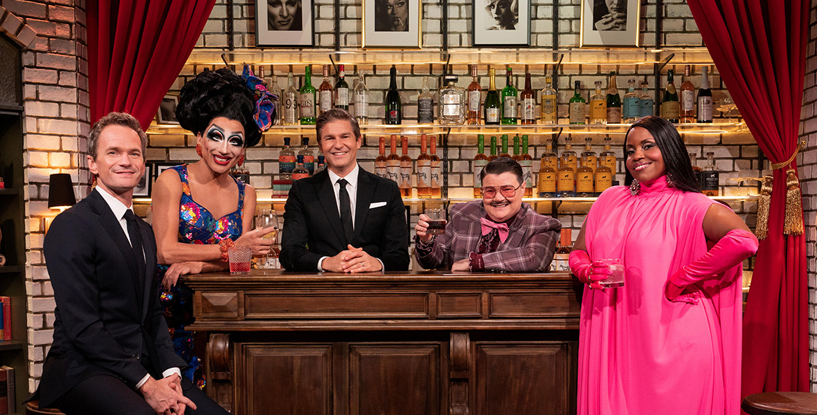 An image from Hulu’s Drag Me to Dinner; from left to right, Neil Patrick Harris, Bianca Del Rio, David Burtka, Murray Hill, and Haneefah Wood are sitting or standing at a bar, smiling at the camera. Harris, Burtka, and Hill are wearing suits; Rio and Wood are wearing evening gowns.