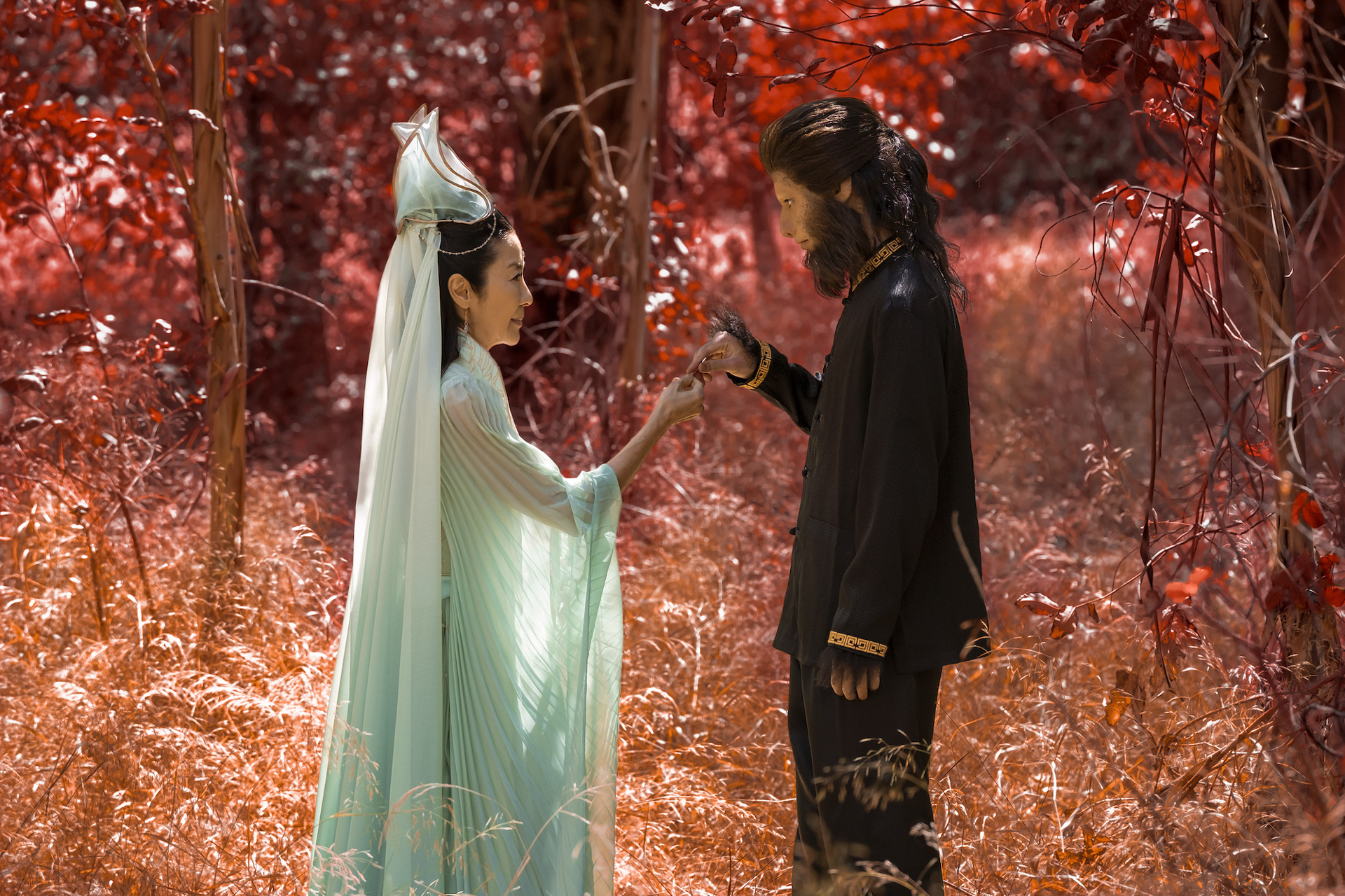 In a scene from American Born Chinese, actors Michelle Yeoh and Jim Liu stand in a tree-covered forest.