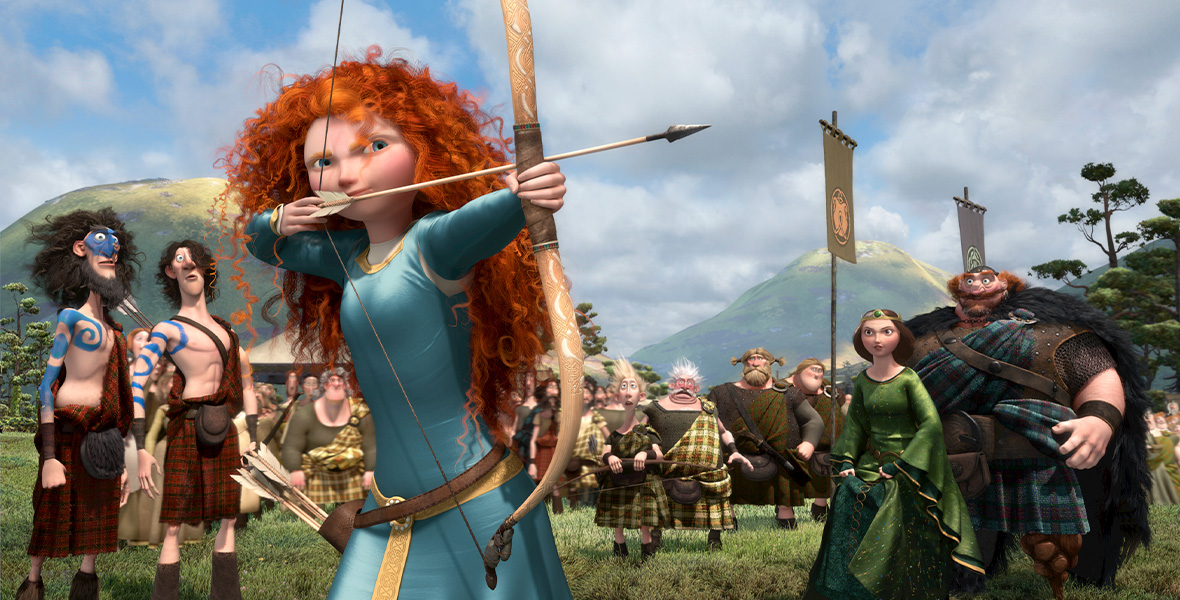 In a scene from Brave, Merida, a teenage girl with red curly hair aims a bow and arrow as a crowd of people watches behind her.
