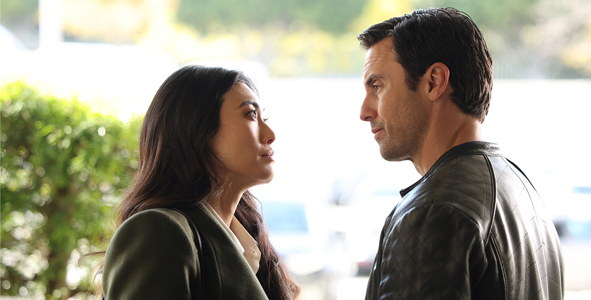 In a scene from The Company You Keep, actors Catherine Haena Kim as Emma and Milo Ventimiglia as Charlie talk closely on a city sidewalk.