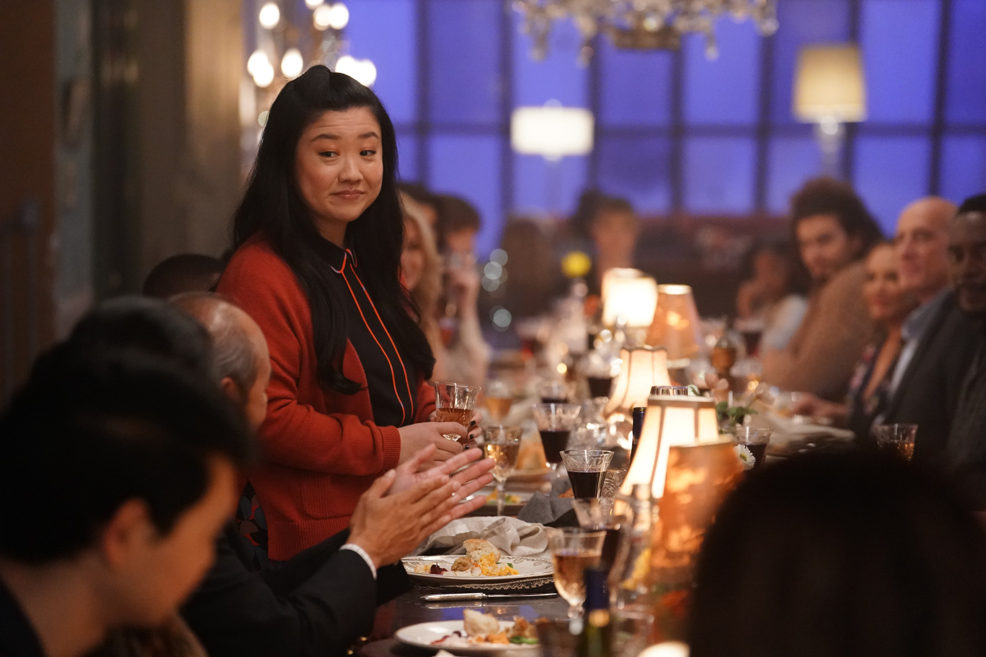 In a scene from Good Trouble, actor Sherry Cola stands and makes a toast during a dinner party.