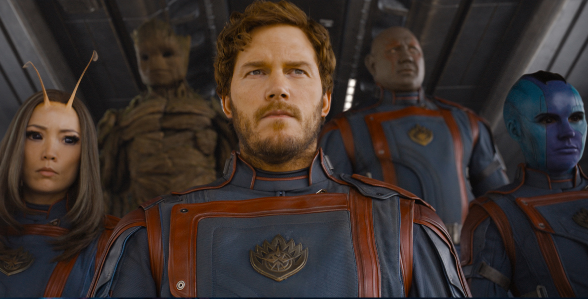 In Guardians of the Galaxy Vol. 3, Peter Quill, Mantis, Nebula, Drax, and Groot stand in a huddled formation and stare forward over the camera. They wear the same solemn expression and red and blue uniforms.