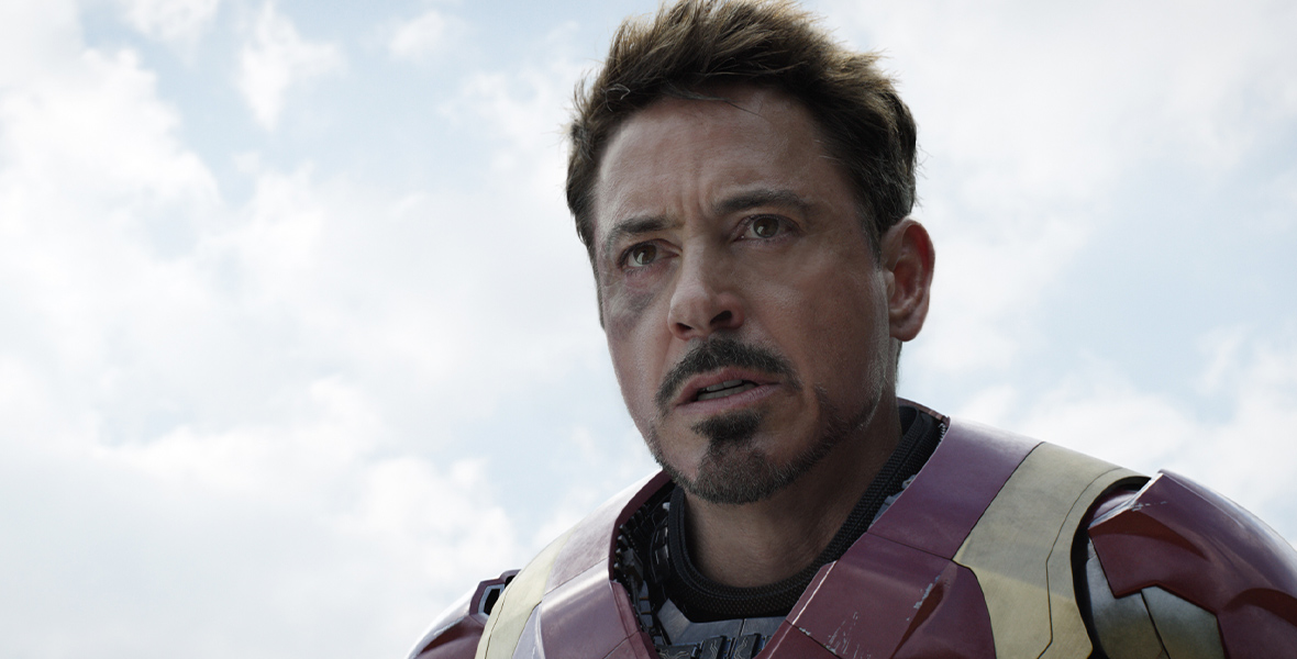 In a scene from Captain America: Civil War, Robert Downey Jr. plays Iron Man. He is wearing a red and gold metal suit. His helmet is off and his right cheek is bruised.