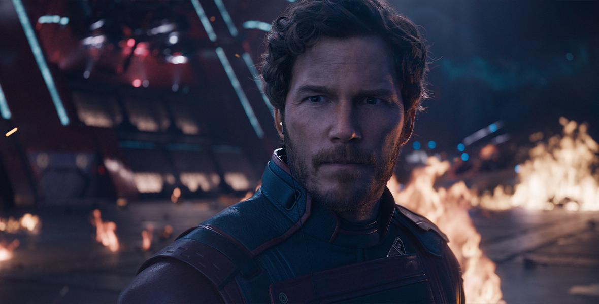 In an image from Marvel Studios’ Guardians of the Galaxy Vol. 3, Peter Quill (Chris Pratt) is looking intently off screen to the left. There is fire behind him, as if a battle has just been waged.