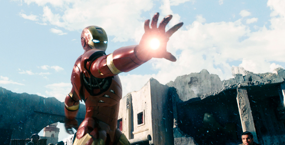 In the Marvel Studios’ film Iron Man, Iron Man stands outside in his red and yellow metallic suit. He braces himself in a fighting pose and holds his right arm out, which emits a bright blast from his hand.
