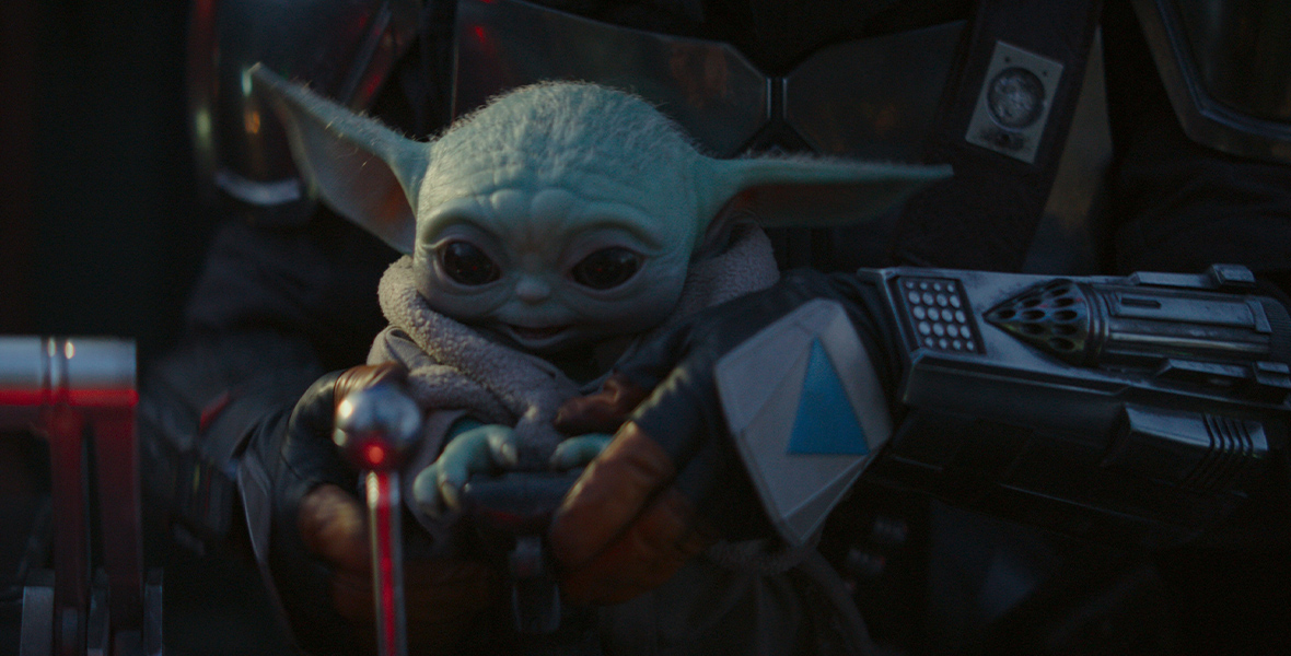 In the Disney+ series The Mandalorian, small green creature Grogu looks at a part of the ship in awe. The Mandalorian holds him in his hands.