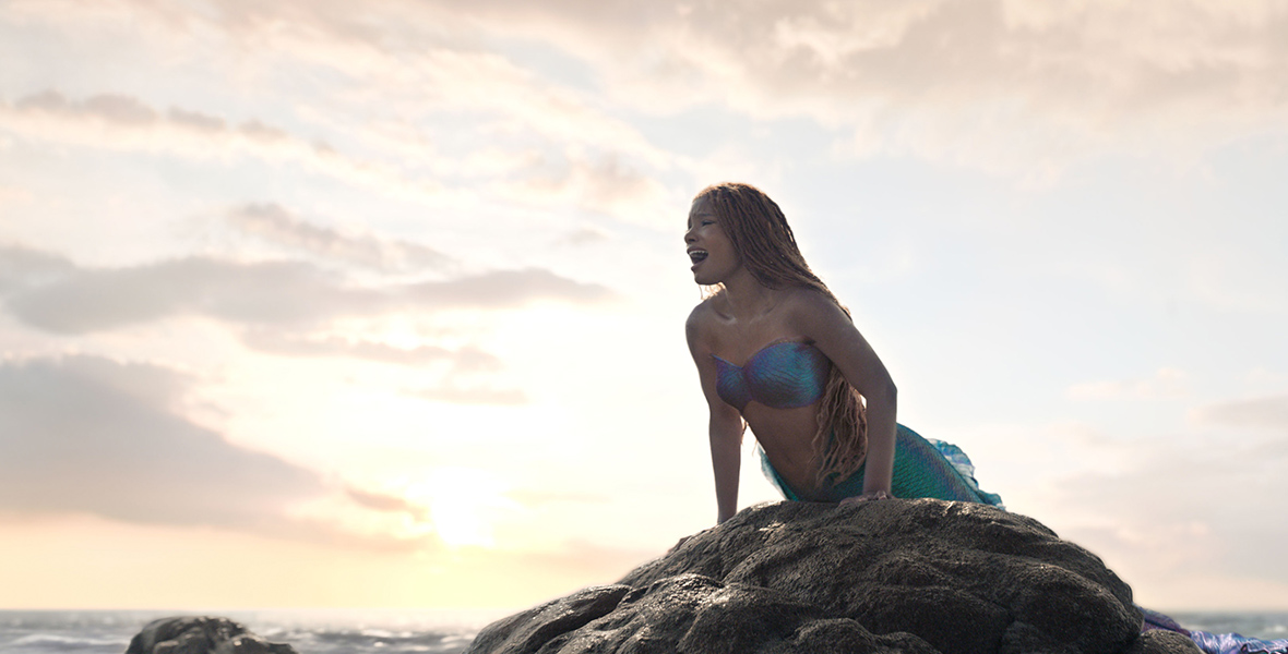 Ariel (Halle Bailey) emerges from the sea, propping herself up on a large rock formation as she sings about her longing to be part of the human world through the famed ballad “Part of Your World” in a scene from the live-action The Little Mermaid.