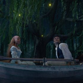 Ariel (Halle Bailey) and Prince Eric (Jonah Hauer-King) sit in a rowboat in an enchanted forest scene at night as Sebastian (Daveed Diggs), Flounder (Jacob Tremblay), and Scuttle (Awkwafina) urge the prince to “Kiss the Girl.”