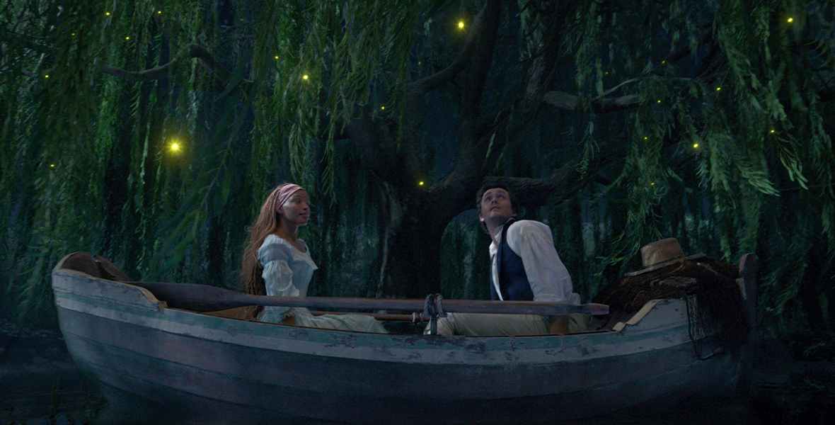 Ariel (Halle Bailey) and Prince Eric (Jonah Hauer-King) sit in a rowboat in an enchanted forest scene at night as Sebastian (Daveed Diggs), Flounder (Jacob Tremblay), and Scuttle (Awkwafina) urge the prince to “Kiss the Girl.”