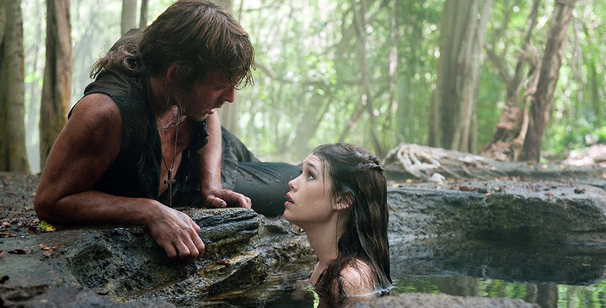 In Pirates of the Caribbean: On Stranger Tides, the dark-haired mermaid Syrena peeks above the surface of a jungle pool to look at Philip, a handsome human, who gazes down at her. He lays on the rock, wearing a vest and a cross hanging on his neck.