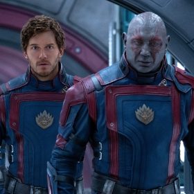 In a still from Marvel Studios' Guardians of the Galaxy Vol. 3, from left to right (and back to front,) Nebula (Karen Gillan), Peter Quill (Chris Pratt), and Drax (Dave Bautista) are walking down a spaceship hallway wearing matching uniforms.