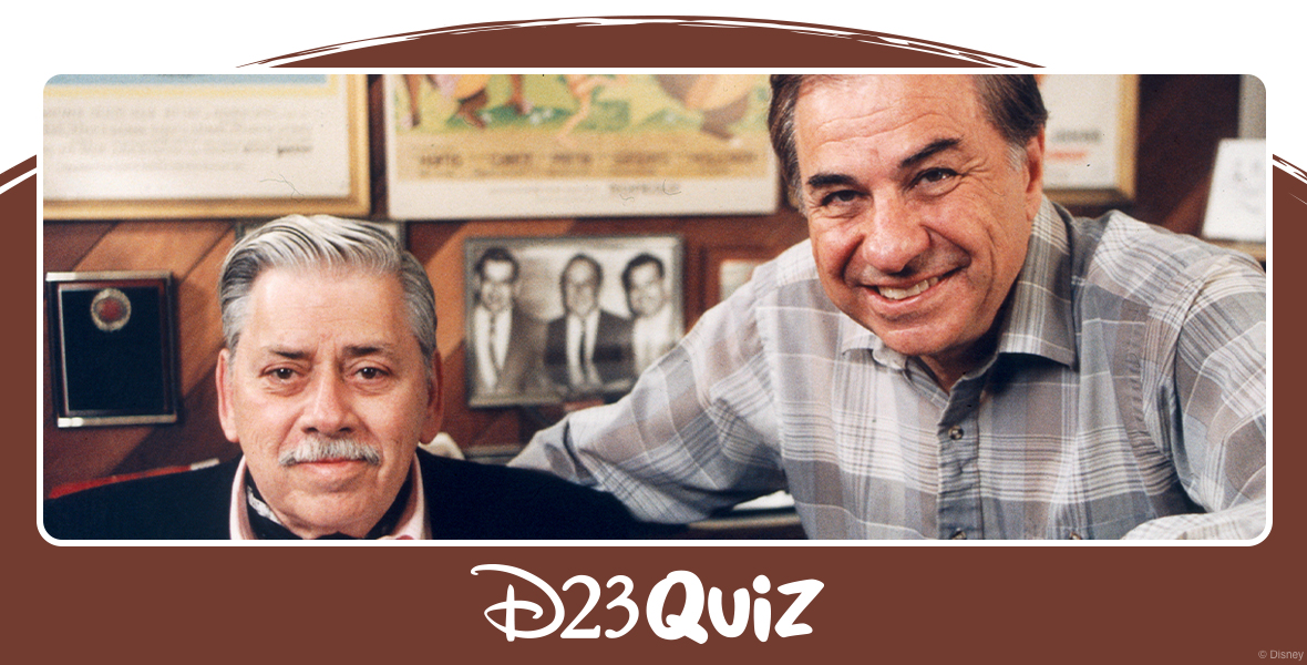 A color photo of Robert and Richard Sherman sitting in front of various posters from their projects. Robert has silvery white hair and a mustache. He’s wearing a light pink button-up shirt, black suit jacket, and black ascot. Richard’s hair is dark brown and he is wearing a gray plaid button-up and has a black wristwatch on his left hand. Behind the brothers you can make out posters for The Jungle Book, Mary Poppins, and Tom Sawyer.