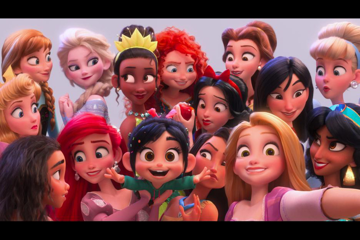 In this image from Ralph Breaks the Internet, a gaggle of Disney Princesses surrounds Vanellope von Schweetz (voiced by Sarah Silverman) as they all take a selfie. Among the princesses, in the upper left-hand corner, are Anna (voiced by Disney Legend Kristen Bell) and Elsa (voiced by Disney Legend Idina Menzel) from Frozen. Other princesses seen include Belle from Beauty and the Beast, Tiana from The Princess and the Frog, and Merida from Brave.