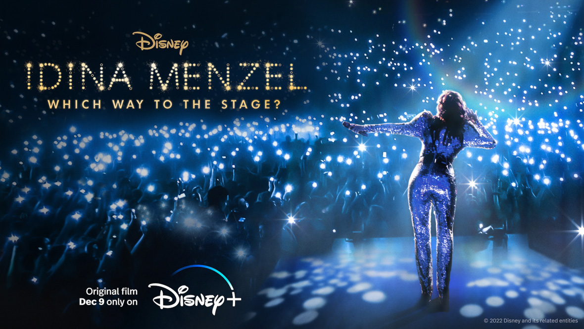 In a promotional image for the documentary special Idina Menzel: Which Way to the Stage?, Disney Legend Idina Menzel is facing away from the camera wearing a sequin jumpsuit, standing on a stage and singing to a large crowd—who are all holding up cellphones that have their flashlights turned on. In one hand, Menzel holds a mic; the other hand is up to her right ear. The name of the special can be seen in the upper left corner of the image.