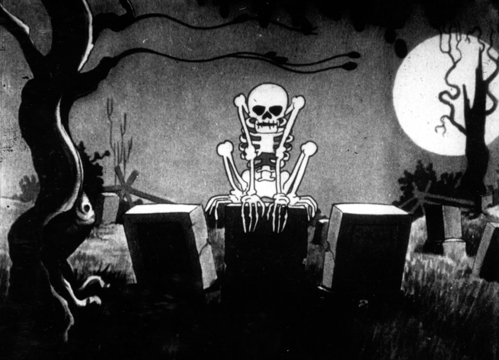 A skeleton hunches over a tombstone in a scene from The Skeleton Dance short.