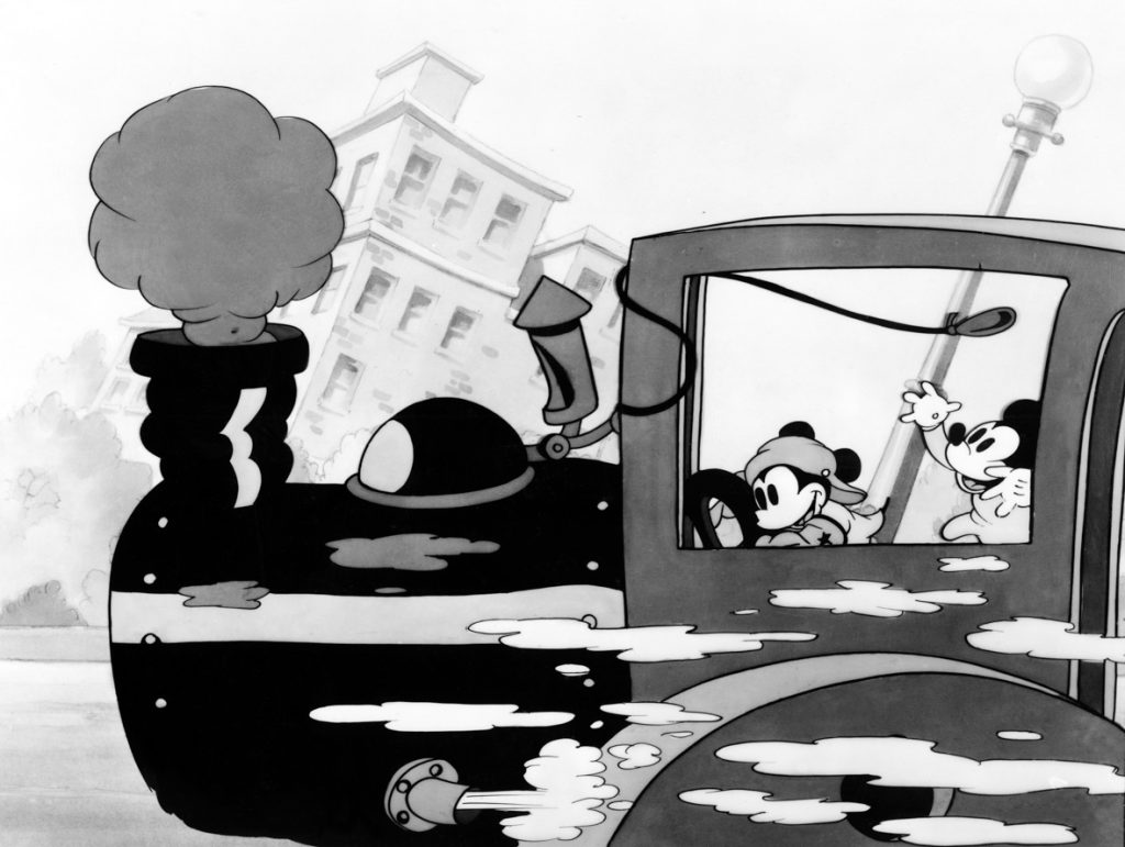 In this image from the animated short Mickey’s Steam Roller, Mickey Mouse drives a speeding steamroller from right to left along a city street. Minnie Mouse is in the cab of the steamroller, behind Mickey. A puff of smoke emerges from the smokestack at the front of the steamroller.