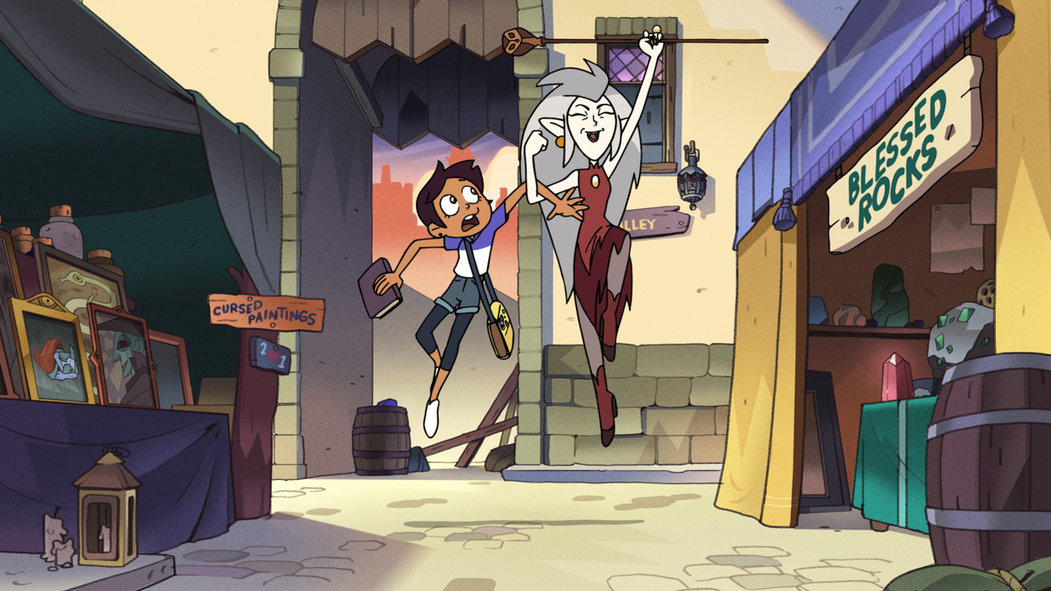 In the animated series The Owl House, teenage Luz and witch Eda link arms and skip down the street. Eda, who has long white hair and wears a red dress and boots, grins and holds a scepter in the air. Luz, who has short brown hair and wears a T-shirt, looks faintly terrified. They’re skipping down the cobbled street of a market, with a shop called “Blessed Rocks” on the right and a stall called “Cursed Paintings” to the left.