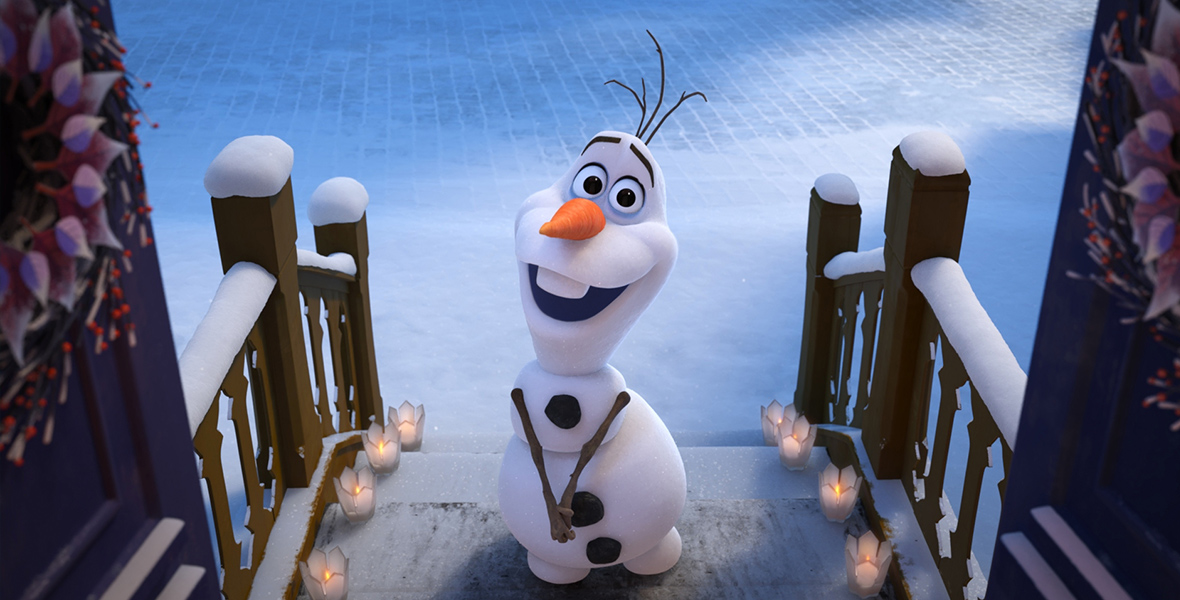 In the animated short Olaf’s Frozen Adventure, snowman Olaf stands on a snowy doorstep. His clasps his branches together in front of him and smiles.