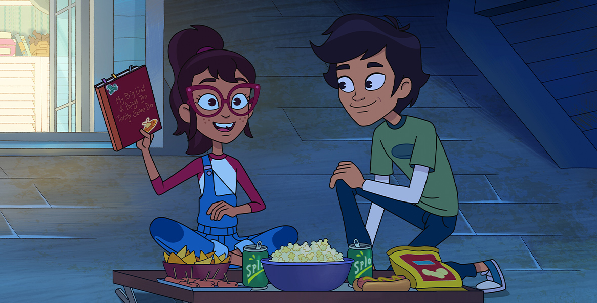 In an image from Disney Channel’s Hailey’s On It!, Hailey (voiced by Auli’i Cravalho) and Scott (voiced by Manny Jacinto) are sitting on the roof of a house; Hailey is holding up a book with an inscription on the cover that says “My Big List of Things I’m Totally Gonna Do.” In front of them is a tray table full of snacks. Hailey is wearing big red glasses and overalls; Scott is wearing a green T-shirt and jeans.